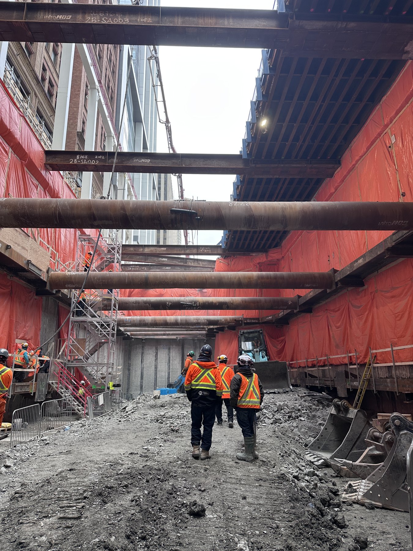Braced excavation with construction crews and red perimeter sheeting