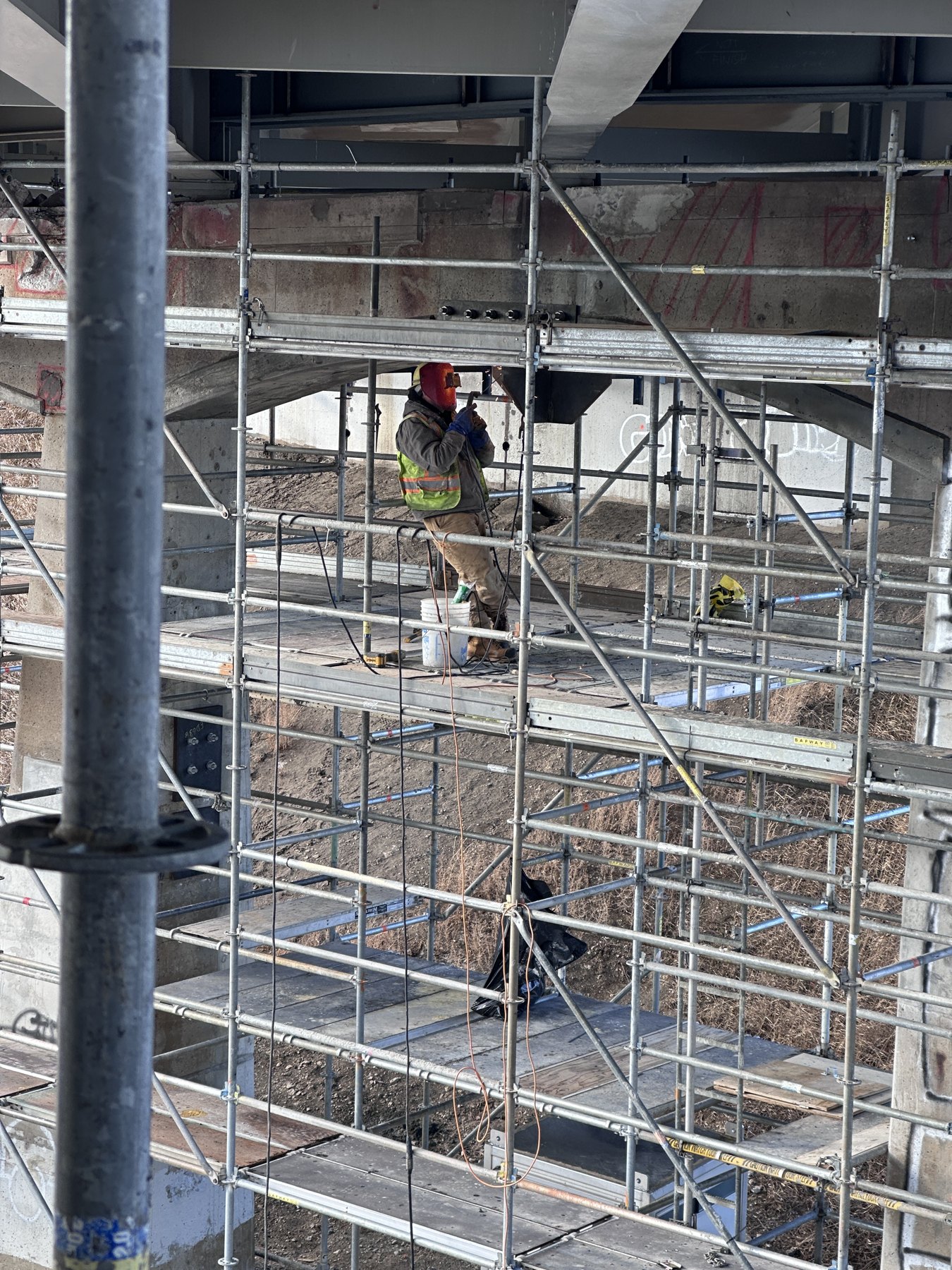 Welder working from scaffolding beneath structural steel